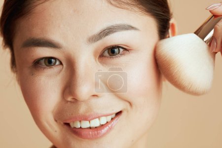 Téléchargez les photos : Young asian female with makeup brush on beige background. - en image libre de droit