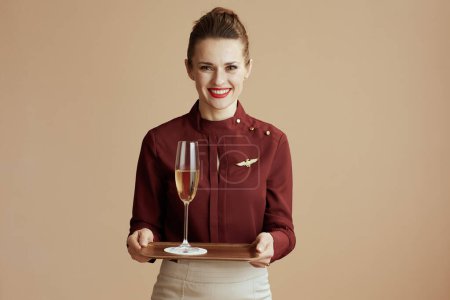 Foto de Happy stylish flight attendant woman against beige background with a glass of champagne. - Imagen libre de derechos