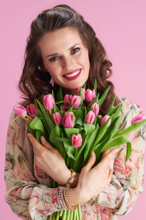 Téléchargez les photos : Portrait de femme heureuse et tendance en robe florale avec bouquet de tulipes sur fond rose. - en image libre de droit