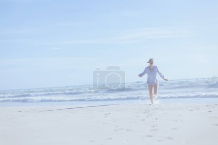 Photo for Full length portrait of smiling elegant middle aged woman at the beach running. - Royalty Free Image