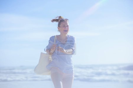 Téléchargez les photos : Heureuse femme élégante avec sac de paille blanche s'amuser à la plage. - en image libre de droit