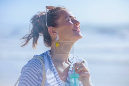 Foto de Happy stylish middle aged woman with drink at the beach. - Imagen libre de derechos