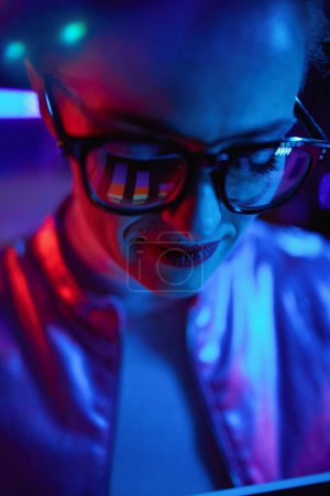 Téléchargez les photos : Neon metaverse concept futuriste. élégante femme de 40 ans avec des graphiques reflétant dans les lunettes dans le bureau moderne. - en image libre de droit
