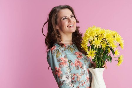 Téléchargez les photos : Happy stylish woman in floral dress with yellow chrysanthemums flowers in vase against pink background. - en image libre de droit