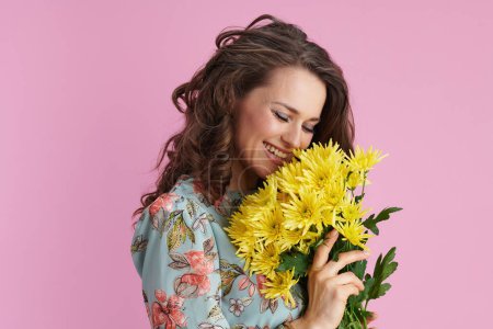 Téléchargez les photos : Femme moderne souriante avec de longs cheveux bruns ondulés avec des fleurs de chrysanthèmes jaunes sur fond rose. - en image libre de droit