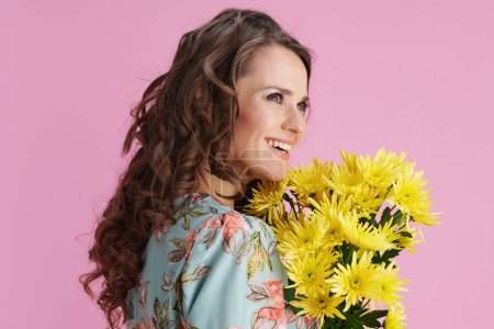 Foto de Mujer de moda feliz con el pelo largo y ondulado morena con flores de crisantemos amarillos aislados sobre fondo rosa. - Imagen libre de derechos