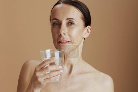 Téléchargez les photos : Femme moderne avec verre d'eau isolé sur fond beige. - en image libre de droit