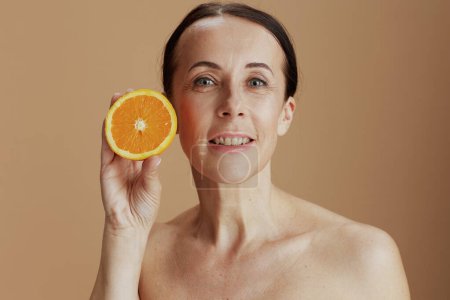 Foto de Happy modern woman with orange on beige background. - Imagen libre de derechos