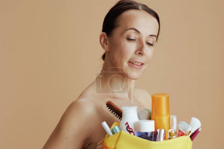 Foto de Modern 40 years old woman with bag of cosmetics against beige background. - Imagen libre de derechos