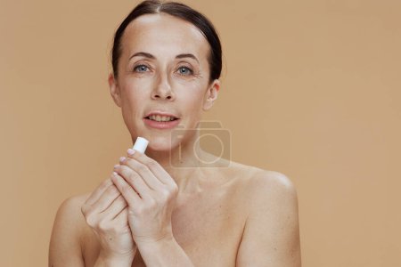 Téléchargez les photos : Modern middle aged woman with hygienic lipstick on beige background. - en image libre de droit