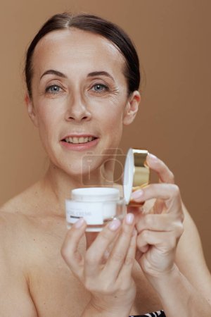 Téléchargez les photos : Portrait of modern 40 years old woman with facial cream jar isolated on beige. - en image libre de droit