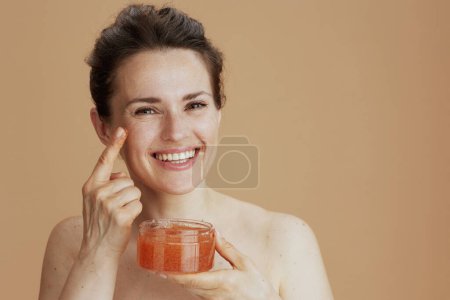smiling middle aged woman with face scrub against beige background.
