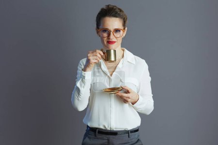 Téléchargez les photos : Young business woman in white blouse with glasses and coffee cup isolated on grey background. - en image libre de droit