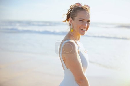 Foto de Portrait of smiling elegant 40 years old woman in white swimwear at the beach. - Imagen libre de derechos