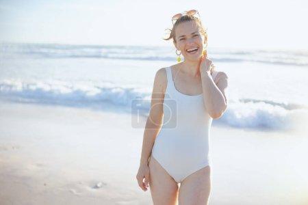 Foto de Sonriente elegante mujer de mediana edad en traje de baño blanco en la playa relajante. - Imagen libre de derechos