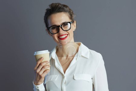 Foto de Feliz de moda 40 años de edad, empleada en blusa blanca con gafas y taza de café aislado sobre fondo gris. - Imagen libre de derechos