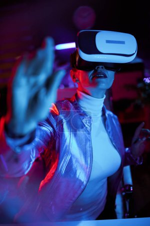 Foto de Concepto futurista neón metaverso. elegante mujer de negocios en gafas de realidad virtual probando metáfora en la oficina moderna. - Imagen libre de derechos
