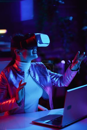 Téléchargez les photos : Neon metaverse futuristic concept. smiling stylish business woman in virtual reality goggles designing metaverse in modern office. - en image libre de droit