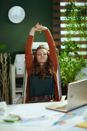 Foto de Relajado elegante dueño de una pequeña empresa mujer con portátil que se extiende en la moderna oficina verde. - Imagen libre de derechos