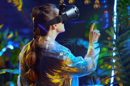 Foto de Seen from behind modern female in virtual reality in vr headset pressing the button in the air. - Imagen libre de derechos