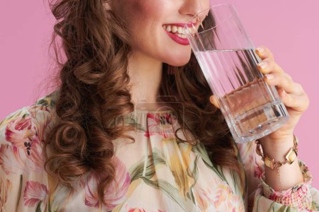 Téléchargez les photos : Closeup on smiling middle aged woman with long wavy brunette hair with glass of water isolated on pink. - en image libre de droit