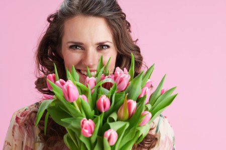 Photo for Portrait of smiling trendy woman in floral dress with tulips bouquet isolated on pink. - Royalty Free Image