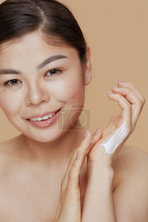 Téléchargez les photos : Portrait de femme asiatique moderne avec crème pour les mains sur fond beige. - en image libre de droit