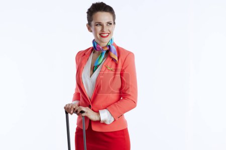 Foto de Smiling stylish flight attendant woman against white background in uniform with trolley bag looking at copy space. - Imagen libre de derechos