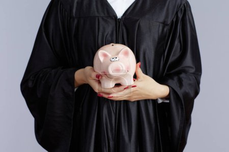Photo for Closeup on young female asian graduate student with piggy bank against grey background. - Royalty Free Image