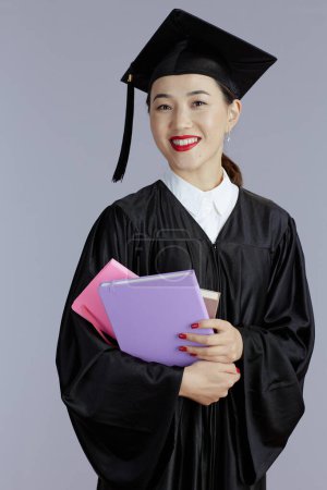 Photo for Smiling modern graduate student asian woman with books and notebooks isolated on gray. - Royalty Free Image