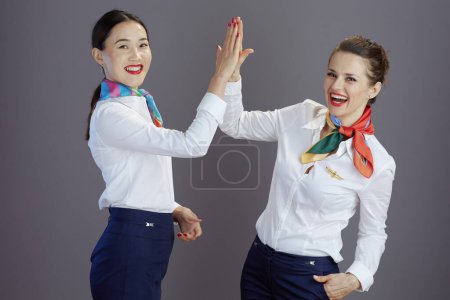 Photo for Smiling modern stewardess women in blue skirt, white shirt and scarf high five isolated on grey. - Royalty Free Image