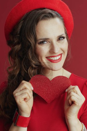 Foto de Feliz San Valentín. Retrato de mujer elegante feliz en vestido rojo y boina sobre fondo rojo con corazón rojo. - Imagen libre de derechos