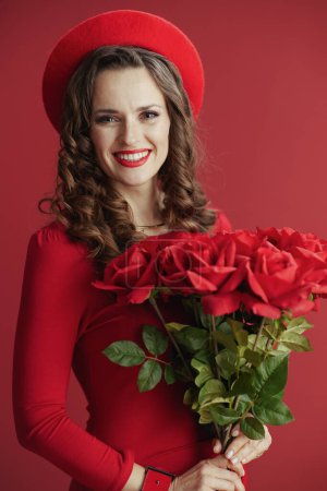Photo for Happy Valentine. happy stylish 40 years old woman in red dress and beret against red background with red roses. - Royalty Free Image