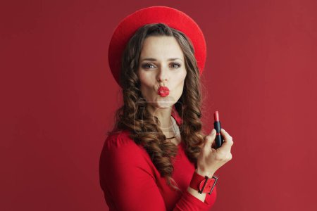 Téléchargez les photos : Joyeux Valentin. élégante femelle en robe rouge et béret isolé sur fond rouge avec rouge à lèvres envoyant un baiser. - en image libre de droit
