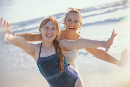 Téléchargez les photos : Portrait de la mère moderne souriante et de la fille adolescente à la plage en vêtements de plage s'amuser. - en image libre de droit