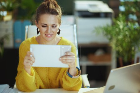 Téléchargez les photos : Heureux élégant propriétaire de petite entreprise femme en pull jaune dans le bureau vert moderne en utilisant tablette PC. - en image libre de droit