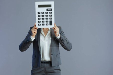 Téléchargez les photos : Élégant employé féminin en costume gris avec calculatrice isolé sur fond gris. - en image libre de droit