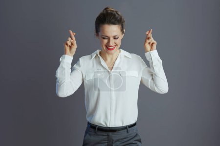 empleada femenina con estilo feliz en blusa blanca con dedos cruzados sobre fondo gris.