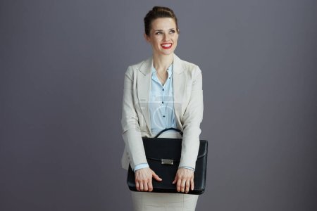 Téléchargez les photos : Heureux élégant femme d'âge moyen employé dans un costume d'affaires léger avec mallette isolée sur gris. - en image libre de droit
