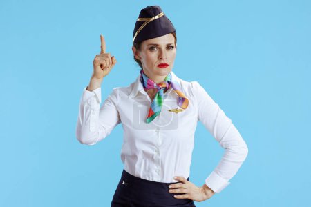 Photo for Elegant air hostess woman isolated on blue background in uniform with raised finger drawing attention. - Royalty Free Image