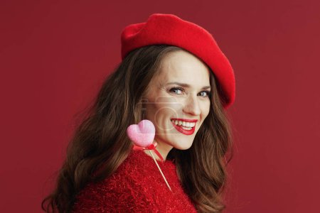 Téléchargez les photos : Joyeux Valentin. souriant femme d'âge moyen à la mode en pull rouge et béret avec coeur sur le bâton. - en image libre de droit