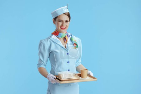 Photo for Smiling modern air hostess woman against blue background in blue uniform with a tray of food. - Royalty Free Image