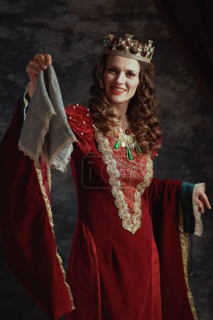 Foto de Feliz reina medieval en vestido rojo con pañuelo y corona sobre fondo gris oscuro. - Imagen libre de derechos