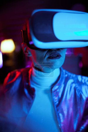 Photo for Neon metaverse futuristic concept. stylish middle aged woman in vr headset on dark background. - Royalty Free Image
