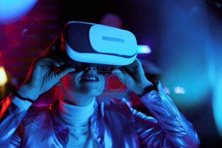 Téléchargez les photos : Neon metaverse concept futuriste. curieuse femelle moderne en réalité virtuelle lunettes sur fond sombre. - en image libre de droit