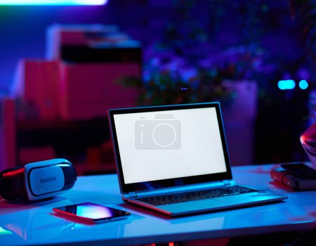 Foto de Concepto futurista neón metaverso. moderna oficina con mesa, tablet PC, laptop con pantalla en blanco y auriculares vr. - Imagen libre de derechos