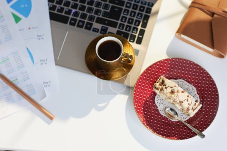 Téléchargez les photos : Concept de santé mentale au travail. Vue supérieure de la table dans un bureau moderne avec morceau de gâteau, tasse de café, documents et ordinateur portable. - en image libre de droit