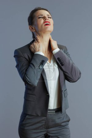 Téléchargez les photos : Stressé tendance 40 ans propriétaire de petite entreprise femme en costume gris ayant douleur au cou sur fond gris. - en image libre de droit