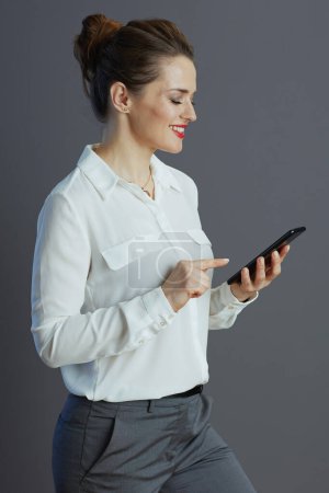 Photo for Smiling stylish female employee in white blouse texting using smartphone isolated on gray. - Royalty Free Image