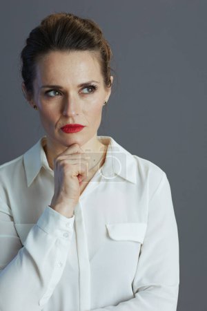 Foto de Pensativo elegante 40 años de edad, mujer trabajadora en blusa blanca mirando a un lado sobre fondo gris. - Imagen libre de derechos